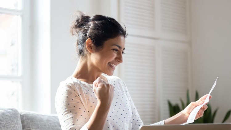 Happy Indian woman reading good news in letter&comma; notification&comma; holding paper&comma; smiling girl rejoicing success&comma; student excited by positive exam results&comma; showing yes gesture&comma; sitting on couch at home