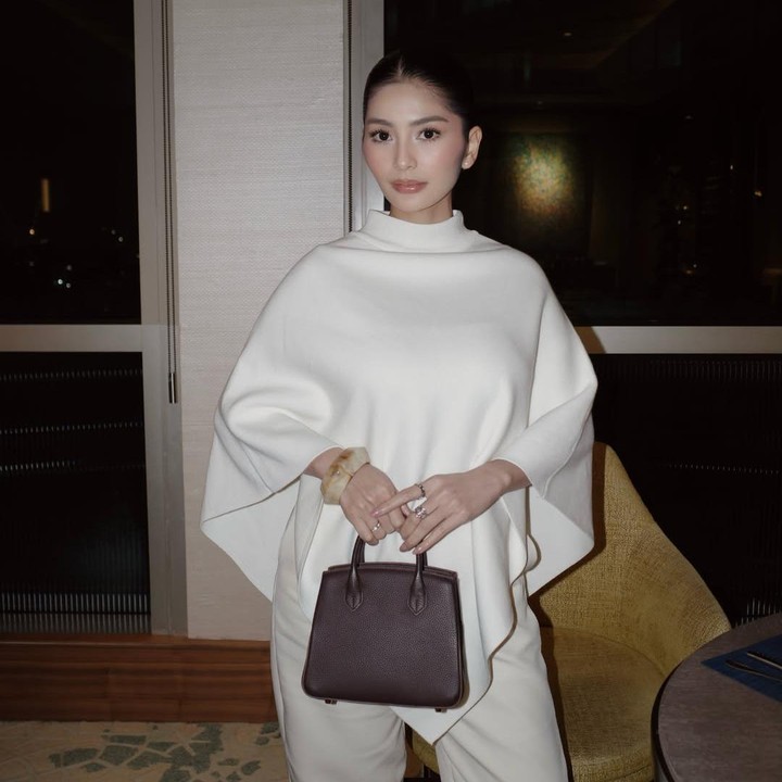 <p>Gaya modis Debi saat hamil juga dapat dilihat saat ia berhasil padu padan <em>cape-style sweater</em> putih dengan celana bahan berwarna senada. Debi melengkapi gayanya dengan <em>handbag</em> cokelat gelap dan aksesoris gelang serta beberapa cincin di jari tangan. Dalam balutan pakaian ini, Debi terlihat glowing karena menonjolkan tampilan less makeup dengan model rambut dikuncir sederhana. (Foto: Instagram @debisagita<em>)</em></p>