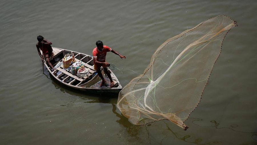 Seorang laki-laki menebar jaring ikan ke perairan sungai Yamuna pada hari musim panas nan terik di New Delhi, India, 25 Mei 2026.
