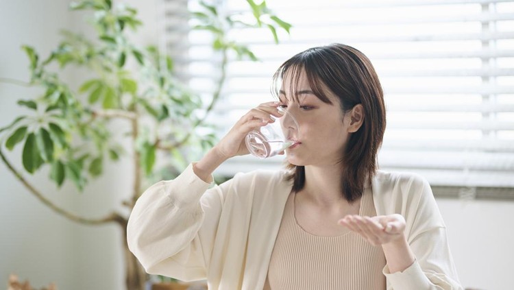 A 20-something woman taking a supplement in bed