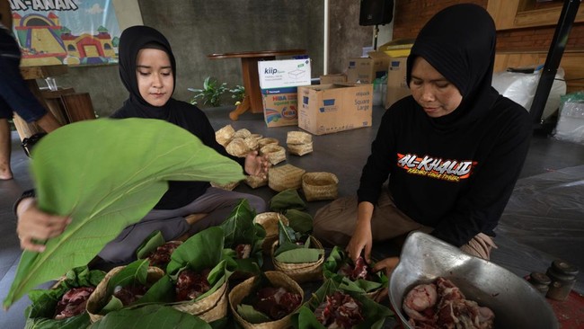 Warga mengemas daging kurban menggunakan besek bambu beralaskan daun jati di Masjid Al-Khalid Kota Kediri, Jawa Timur, Rabu (27/5/2026). Pemanfaatan besek dan daun jati sebagai pembungkus daging kurban tersebut sebagai upaya mendukung program pemerin