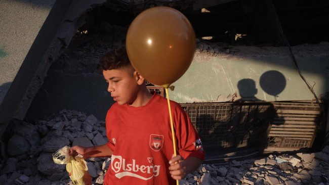 The shadow of a Palestinian boy holding a balloon is cast on the ruins of a destroyed building during morning prayers marking the start of Eid al-Adha, the Feast of Sacrifice, in Khan Yunis in the southern Gaza Strip on May 27, 2026. Since October 10