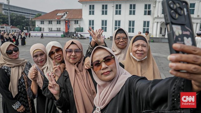 Sejumlah wisatawan membawa payung saat mengunjungi Kota Tua, Jakarta Barat, Sabtu (30/5/2025) siang. (CNN Indonesia/Febria Adha L)