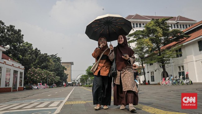 Sejumlah wisatawan membawa payung saat mengunjungi Kota Tua, Jakarta Barat, Sabtu (30/5/2025) siang. (CNN Indonesia/Febria Adha L)