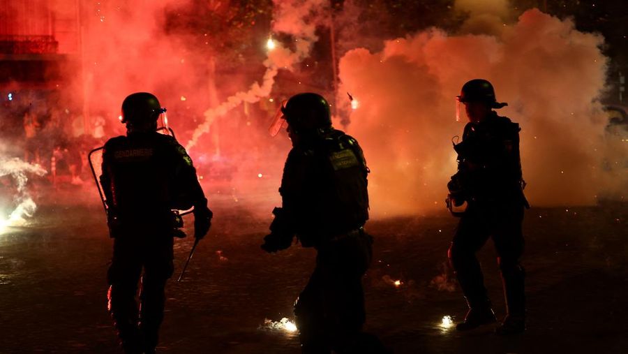 Petugas kepolisian berlindung dari suar nan dinyalakan massa saat seremoni kemenangan Paris Saint-Germain usai menjuarai Liga Champions UEFA di Paris, Minggu (31/5/2026). (REUTERS/Abdul Saboor)