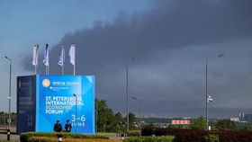 Police officers stand in front of a banner and flags with the logo of the St. Petersburg International Economic Forum (SPIEF) as heavy smoke billows in the background after Ukrainian drones hit infrastructure, according to the governor Alexander Begl