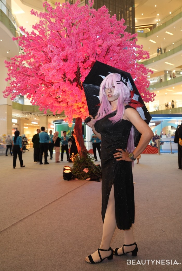 Cosplayer ini tampil cantik dengan gaun hitam dan heels-nya. Bak perempuan di karakter anime, ia menambahkan wig berwarna merah muda.