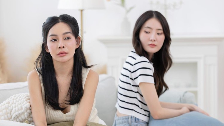Two angry asian female friends sitting separately on sofa after having a big fight