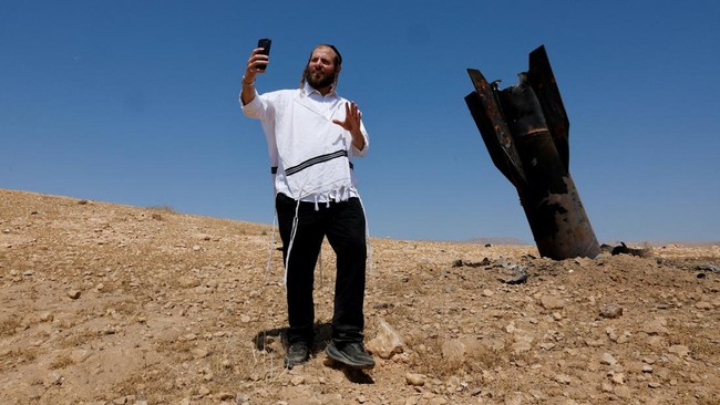An Israeli ultra-Orthodox Jewish man takes a selfie near a part of a missile protruding from the ground, following strikes from Iran, in the central Israeli-occupied West Bank, June 8, 2026. REUTERS/Ammar Awad