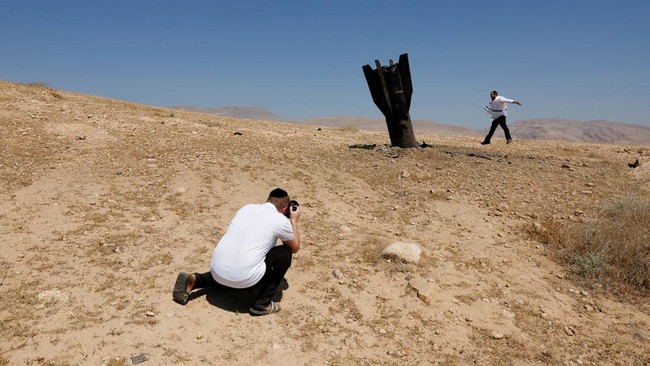 A person takes a photo of an Israeli ultra-Orthodox Jewish man reacting near a part of a missile protruding from the ground, following strikes from Iran, in the central Israeli-occupied West Bank, June 8, 2026. REUTERS/Ammar Awad
