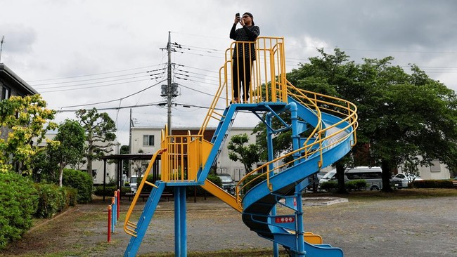 A person uses their phone while standing on top of a playground slide as police officers search for a black bear that was spotted at a residential area in Utsunomiya, Tochigi Prefecture, Japan, June 9, 2026. REUTERS/Kim Kyung-Hoon
