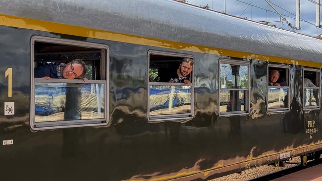 Passengers lean out of window at a station stop, aboard the