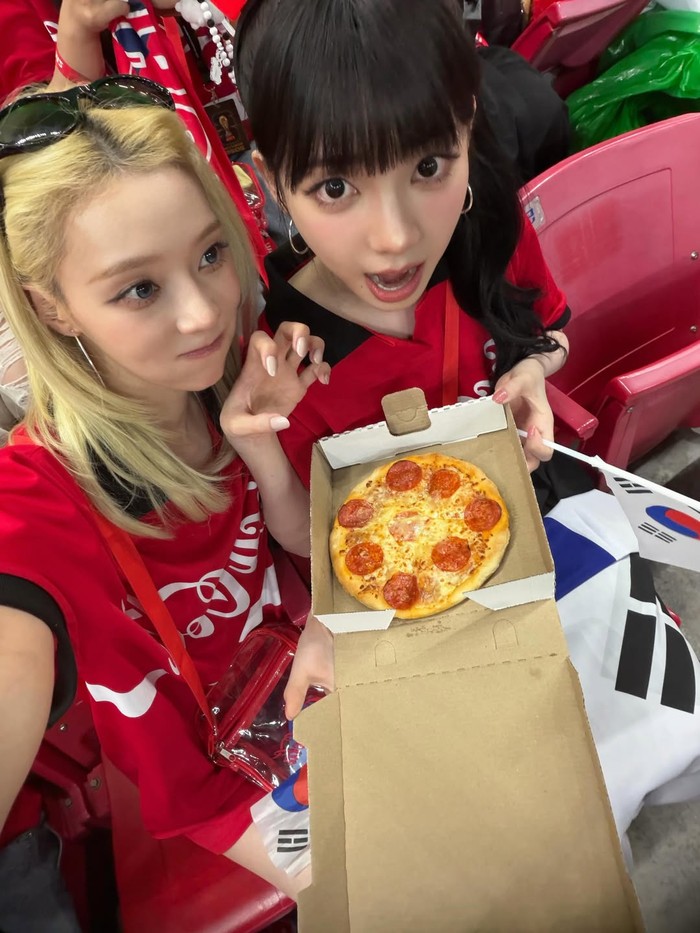 Bak supporter sepak bola, Karina dan Winter kompak menunjukkan gaya sporty namun tetap modis dengan jersey merah berlogo Coca-Cola, sambil menyantap pizza di tengah keramaian tribun./ Foto: instagram.com/imwinter