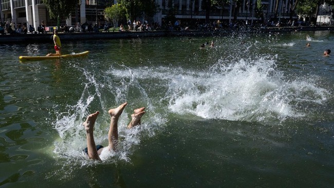 Young people dive into the Bassin des Recollets on the Canal Saint-Martin in Paris on June 17, 2026. France braced for another heat wave on June 17, with Paris allowing swimming in one of its canals so residents could cope with the heat. (Photo by JO