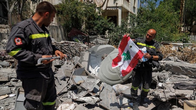 A member of the government-run Lebanese Civil Defense, the country's primary firefighting, first aid, and rescue force, holds a Lebanese flag salvaged from the rubble while inspecting their headquarters in Nabatieh, Lebanon, June 17, 2026, following