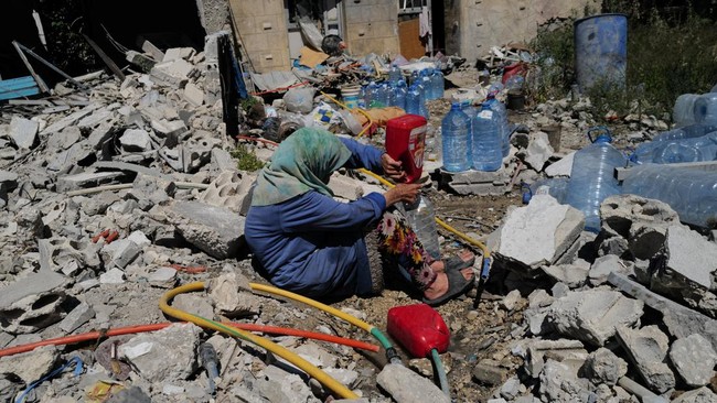 Khadija Amara, whom local residents said had not left her home, fills a jerrycan with water as she sits among the rubble of a house, which was damaged by an Israeli strike, in Qlaileh in the Tyre district, southern Lebanon, June 19, 2026. REUTERS/Zoh