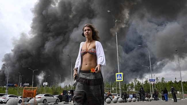 A woman walks outside a shopping mall as black smoke rises from the area of the Russian oil producer Gazprom Neft's Moscow oil refinery on the south-eastern outskirts of Moscow on June 18, 2026. Moscow was fending off a