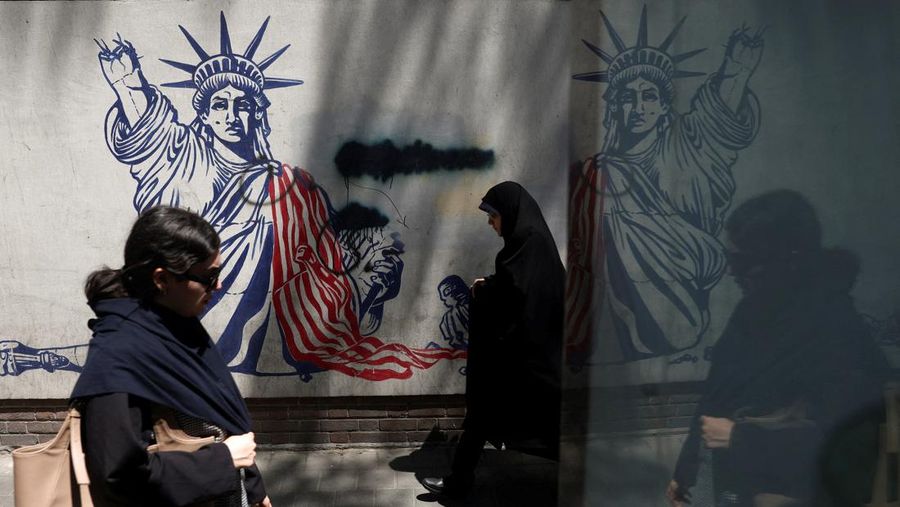 Perempuan Iran melangkah melewati mural anti-AS di sebuah jalan di Teheran, Iran, Senin (15/6/2026). Meski hidup dalam ketidakpastian, sebagian penduduk Iran berupaya menjalani hari seperti biasa. (via REUTERS/Majid Asgaripour)