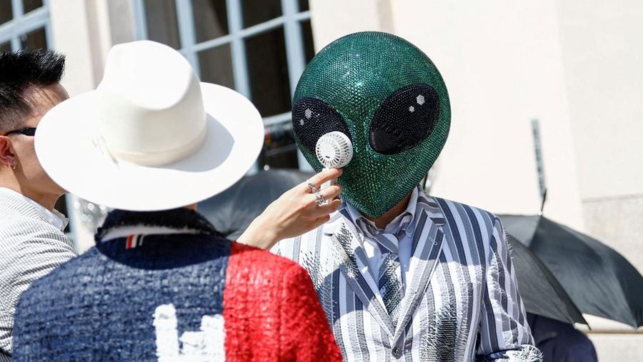 Seseorang nan mengenakan topeng alien duduk di antara penonton dengan kipas angin listrik portabel selama peragaan koleksi busana laki-laki Musim Semi/Musim Panas 2027 karya Thom Browne sebagai bagian dari Milan Fashion Week, di Milan, Italia, 22 Juni 2026.