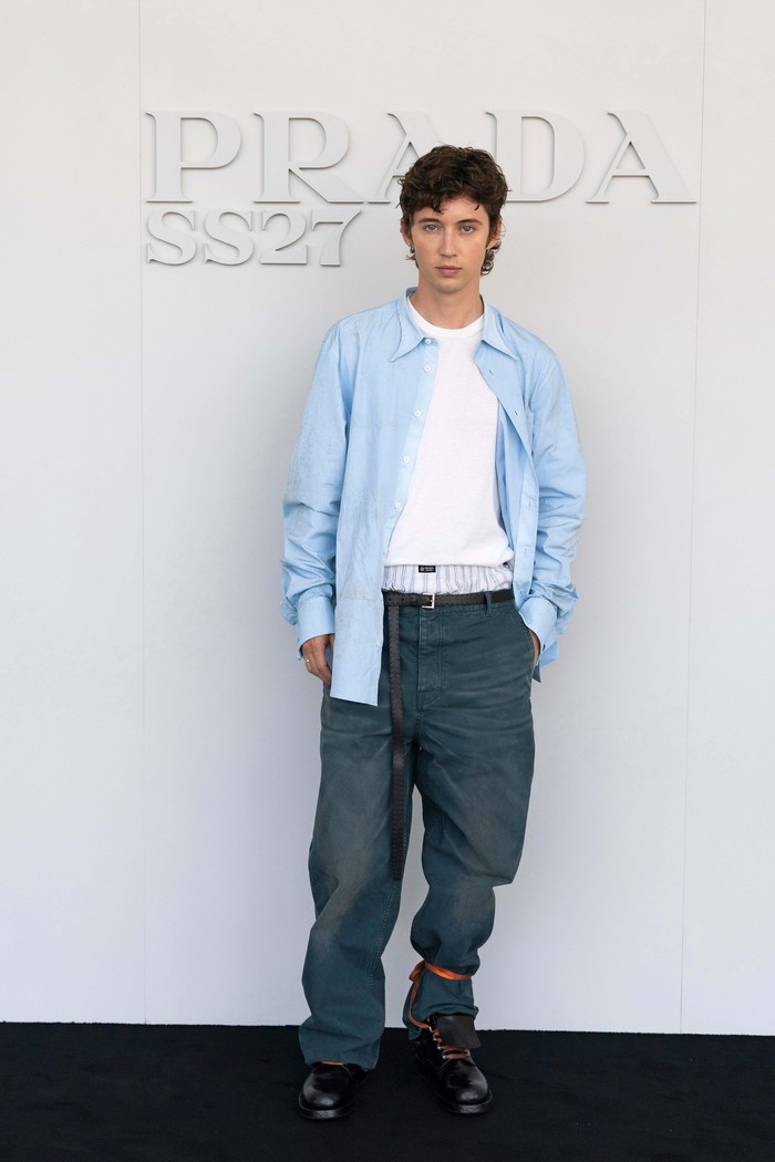 Nuansa laidback didapatkan dari penampilan Troye Sivan. Padanan t-shirt putih polos dengan kemeja biru sebagai luaran, kemudian dikombinasi celana panjang terlihat kasual. Namun detail seperti boxer dan&nbsp;pita&nbsp;oranye yang sengaja diikat pada salah satu kaki menuai atensi tersendiri/ Foto: Dok. Prada