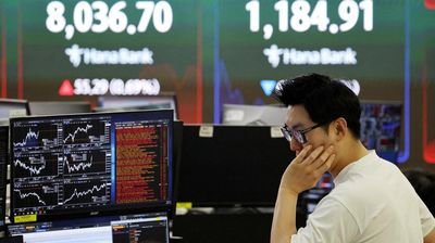 FILE PHOTO: FILE PHOTO: A currency dealer works as an electronic board displays the Korea Composite Stock Price Index (KOSPI) and the Korea Securities Dealers Automated Quotations (KOSDAQ), at the dea