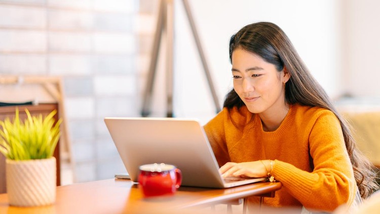 A young woman is using a laptop comfortably in the living room at home&period;
