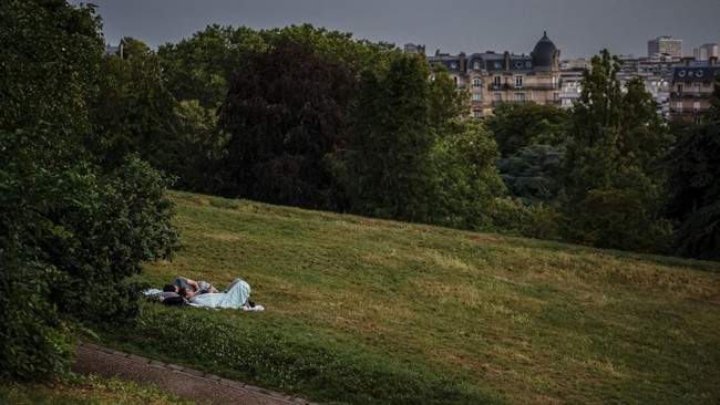 People have a rest on the grass seeking shelter from the heat in the Parc des Buttes-Chaumont in Paris, early June 26, 2026, as France experiences a heatwave. Hundreds of Parisians seeking relief from the heat took refuge in the Parc des Buttes-Chaum