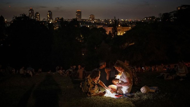 People chat as they shelter from the heat in the Parc des Buttes-Chaumont in Paris, late June 25, 2026, as France experiences a heatwave. Hundreds of Parisians seeking relief from the heat took refuge in the Parc des Buttes-Chaumont, in the north-eas