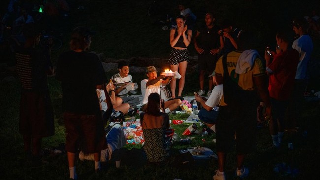 A young man (C) holds a cake while celebrating his birthday with his friends as they shelter from the heat in the Parc des Buttes-Chaumont in Paris, late June 25, 2026, as France experiences a heatwave. Hundreds of Parisians seeking relief from the h