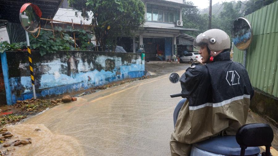Seseorang nan mengendarai skuter menunggu di pinggir jalan nan tergenang air setelah hujan deras akibat Badai Tropis Mekkhala menyebabkan banjir di Hsinchu, Taiwan, 26 Juni 2026.