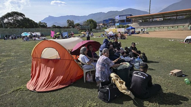 Residents sit beside belongings as they take shelter on a stadium following an earthquake in Catia La Mar, La Guaira state, about 30 km northwest of Caracas, on June 25, 2026. A twin earthquake that was Venezuela's largest in over a century has kille