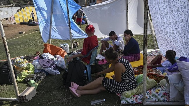 Displaced residents sit on mattresses laid out on a sports field with belongings gathered around them following an earthquake in Catia La Mar, La Guaira state, about 30 km northwest of Caracas, on June 25, 2026. A twin earthquake that was Venezuela's