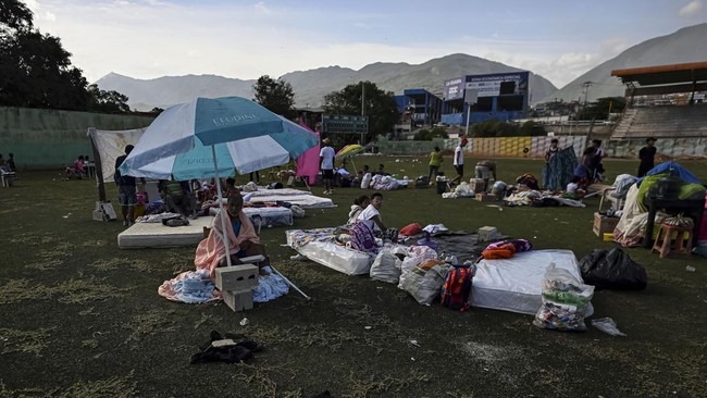 Displaced residents sit on mattresses laid out on a sports field with belongings gathered around them following an earthquake in Catia La Mar, La Guaira state, about 30 km northwest of Caracas, on June 25, 2026. A twin earthquake that was Venezuela's