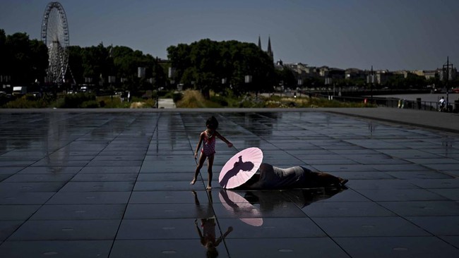 (FILES) A young girl plays in the water of the Mirroir d'Eau reflecting pool to cool down in Bordeaux, southwestern France on June 23, 2026, as France experiences a heatwave. To face the intensity of the record-breaking heatwave scorching Europe, peo