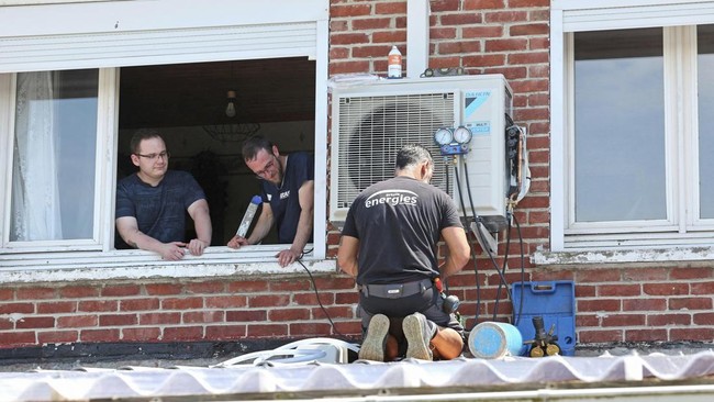 Heating engineers work on installing an air conditioning unit in the home of a local resident (L) in Mericourt, northern France on June 19, 2026.
