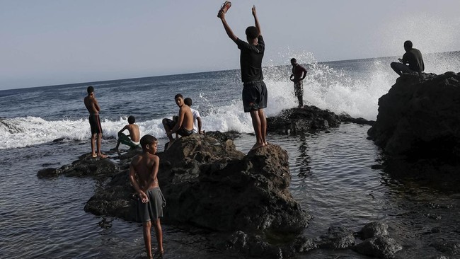 People look on as waves crash over rocks along the shore at Kebra Kanela in Gamboa, Praia, Cape Verde, June 28, 2026. REUTERS/Sodiq Adelakun