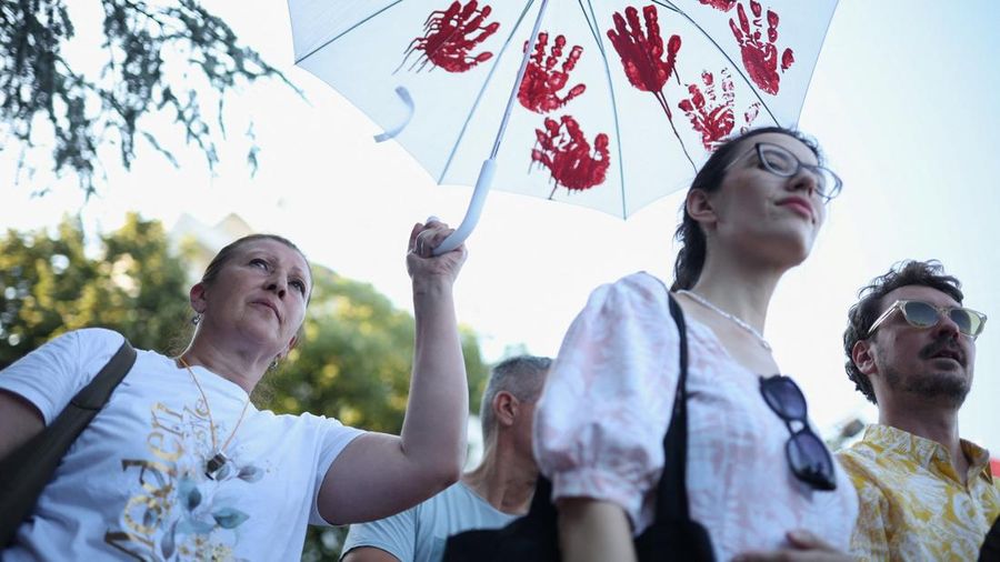 Seorang demonstran memegang payung dengan cetakan tangan cat merah sementara orang-orang berkumpul untuk protes sebagai bagian dari aktivitas anti-pemerintah nasional nan dipicu oleh runtuhnya kanopi stasiun kereta api Novi Sad nan menewaskan banyak orang pada November 2024, menyusul pengumuman pengunduran diri Presiden Serbia Aleksandar Vucic, di Kraljevo, Serbia, 28 Juni 2026.