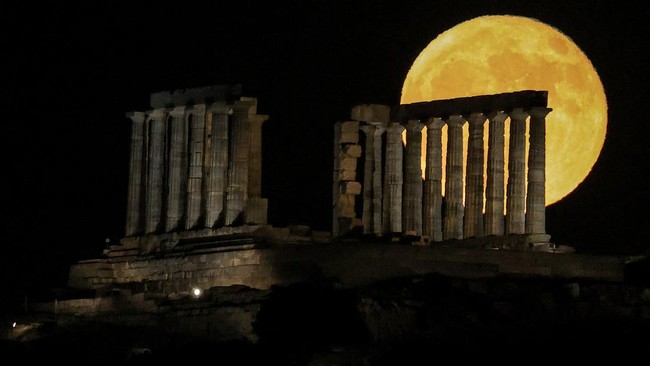 Bulan purnama 'Strawberry' terbit di atas Kuil Poseidon kuno di Tanjung Sounion, sebelah selatan Athena, Yunani, pada 30 Juni 2026. (REUTERS/Louisa Gouliamaki)