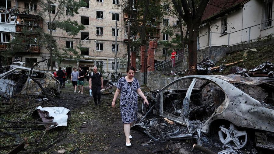 Warga melangkah melewati mobil-mobil nan gosong terbakar akibat serangan rudal dan pesawat tak berawak Rusia semalam, di tengah serangan Rusia terhadap Ukraina, di Kyiv, Ukraina, 2 Juli 2026.