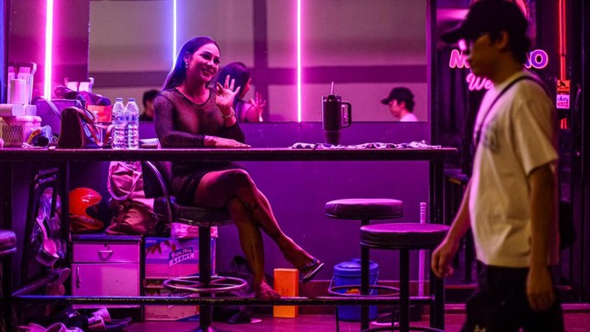 People walk past bars and clubs along a street in Pattaya on July 2, 2026. Scantily dressed and wearing stiletto heels, hundreds of girls, some apparently very young, form a seedy guard of honour under the lights of Soi 6, a street in one of Pattaya'