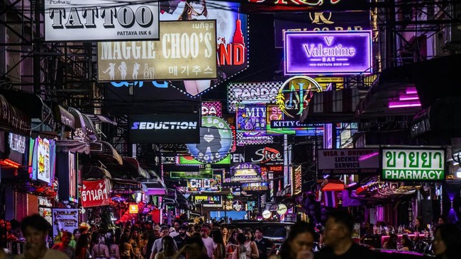 People walk past bars and clubs along a street in Pattaya on July 2, 2026. Scantily dressed and wearing stiletto heels, hundreds of girls, some apparently very young, form a seedy guard of honour under the lights of Soi 6, a street in one of Pattaya'
