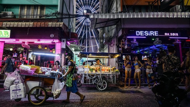 People walk past bars and clubs along a street in Pattaya on July 2, 2026. Scantily dressed and wearing stiletto heels, hundreds of girls, some apparently very young, form a seedy guard of honour under the lights of Soi 6, a street in one of Pattaya'