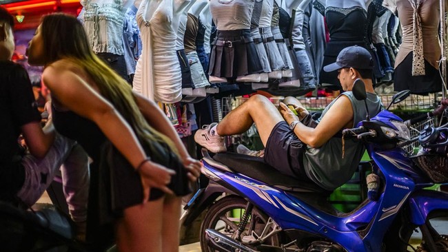 People walk past bars and clubs along a street in Pattaya on July 2, 2026. Scantily dressed and wearing stiletto heels, hundreds of girls, some apparently very young, form a seedy guard of honour under the lights of Soi 6, a street in one of Pattaya'