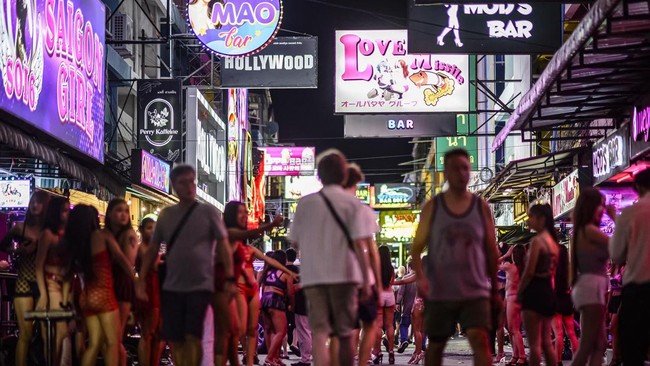 People walk past bars and clubs along a street in Pattaya on July 2, 2026. Scantily dressed and wearing stiletto heels, hundreds of girls, some apparently very young, form a seedy guard of honour under the lights of Soi 6, a street in one of Pattaya'