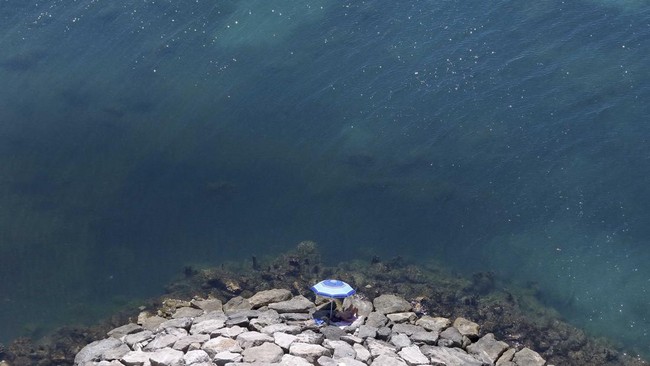 This aerial photograph shows a man sunbathing on rocks in front of the sea in Durres, western Albania, on June 29, 2026. According to the European Union's Copernicus Marine Service, the world's oceans just experienced their hottest June on record, gl