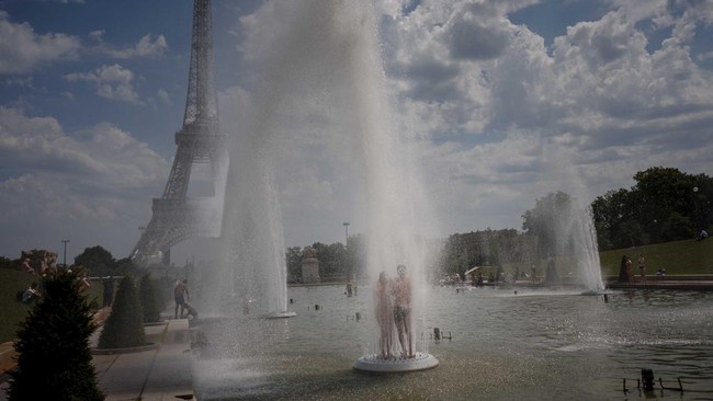 A couple cools off in the Trocadero Fountain with the Eiffel Tower on the background during a heatwave in Paris on June 26, 2026. (Photo by Dimitar DILKOFF / AFP)