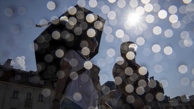 People shelter from the sun under umbrellas as they walk on the Royal Castle Square in Warsaw's Old Town as thermometers show record temperatures during a heatwave that has reached Poland on 28 June 2026 (Photo by Wojtek RADWANSKI / AFP)