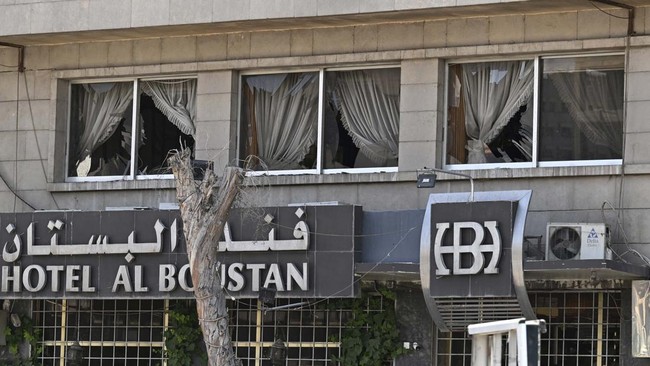 The shattered windowpanes of a hotel are pictured following two blasts in Damascus on July 7, 2026. Two explosions shook Damascus on July 7 near a hotel where French President Emmanuel Macron was staying, wounding at least 18 people, during the Frenc