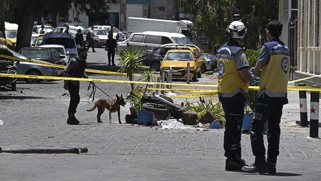 A security personnel along with a sniffer dog inspects near the Four Seasons Hotel following two blasts, in Damascus on July 7, 2026. Two explosions shook Damascus on July 7 near a hotel where French President Emmanuel Macron was staying, wounding at