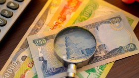 A magnifying glass focuses on a 250 Iraqi Dinar banknote featuring the Malwiya Tower. Various denominations, including 50,000, 25,000, and 10,000 Dinar notes, are scattered on a wooden surface next to a calculator, suggesting financial analysis.